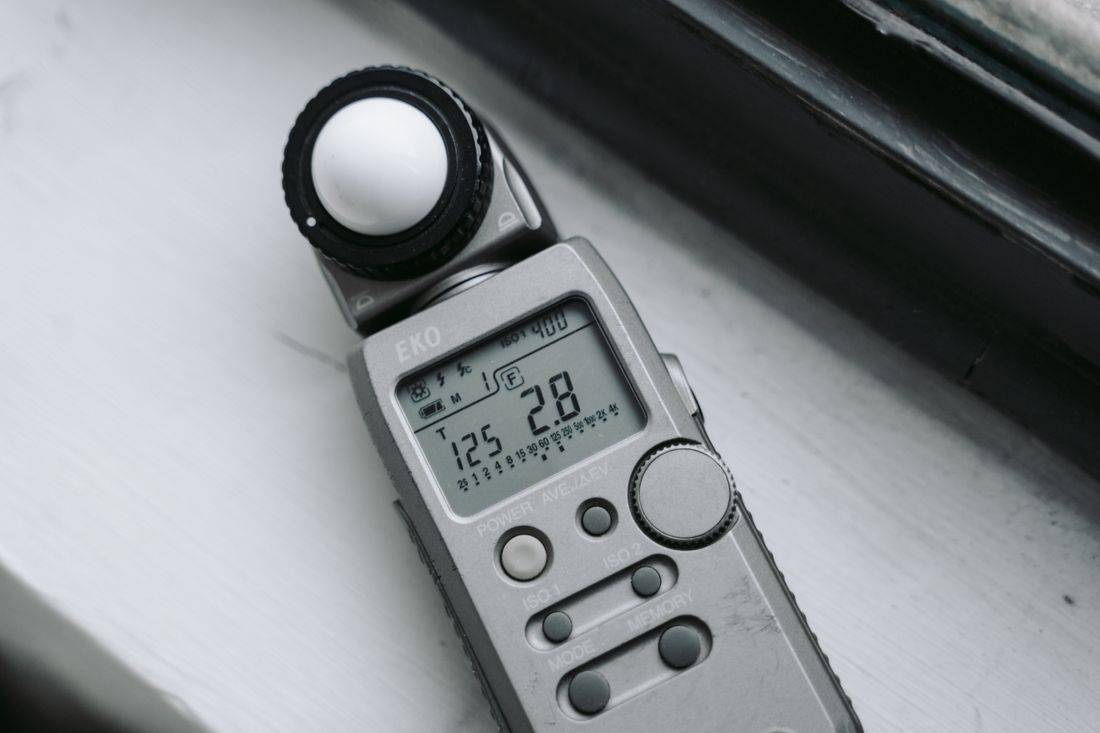 A handheld incident light meter lying on a windowsill, its display showing a shutter speed and an aperture rather than an illuminance value