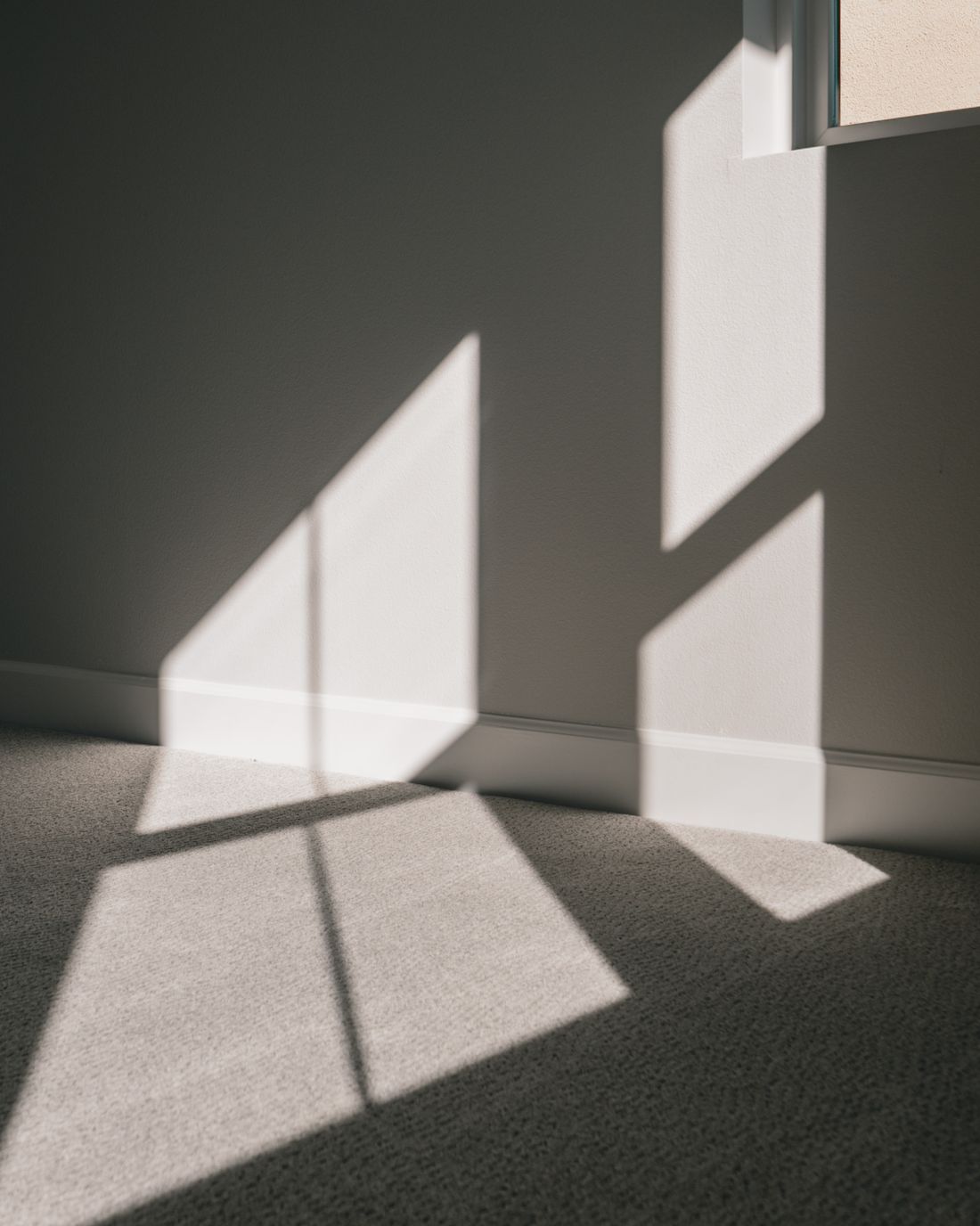 A hard-edged patch of sunlight thrown by a window onto the wall and carpet of an otherwise empty room