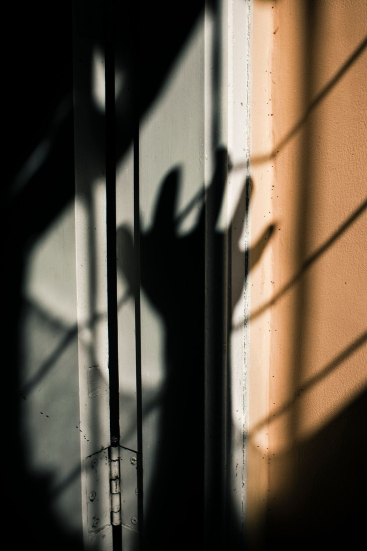 A hand held up in direct sunlight beside a window, throwing a hard-edged shadow with clearly separated fingers onto the wall